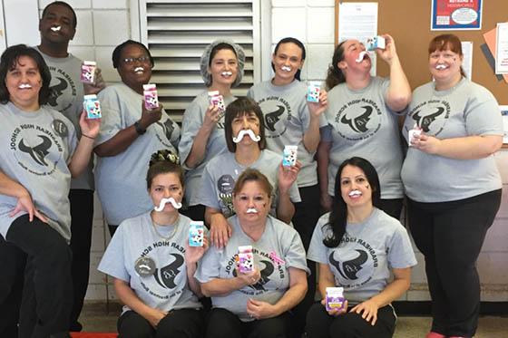 Photo of a group of volunteers wearing the same grey shirt, with fake milk mustaches, each holding a small carton of milk